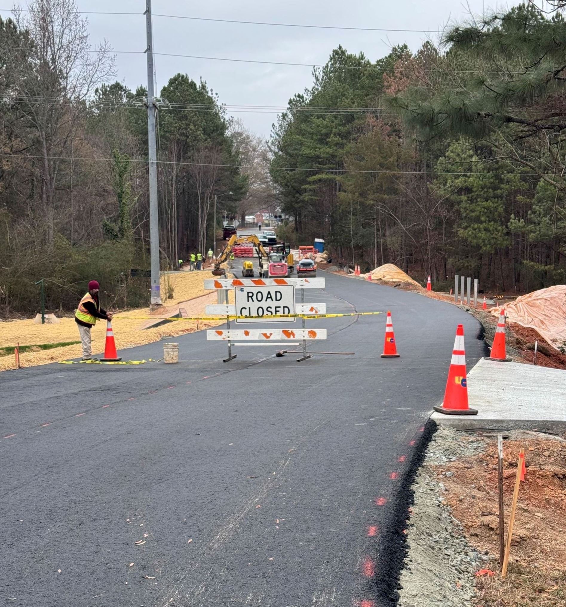 First layer of asphalt newly installed at Pinedell Avenue, worker with road closed sign.